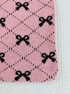 Close-up of pink knitted fabric featuring black bow patterns and diamond grid texture