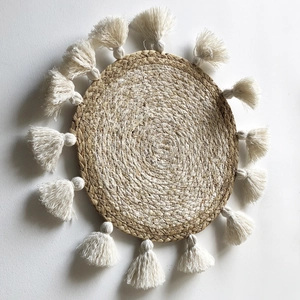 Dettaglio di decorazione murale bohémien in paglia intrecciata con nappe in cotone bianco