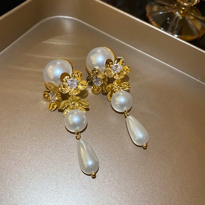 Detailed shot of gold floral earrings with tassels and teardrop pearls on a tray