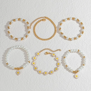 Detail of 6pcs gold chain bracelet set with white pearls and daisy charms on white surface