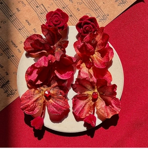 Detail shot of oversized red velvet flower earrings with crystals on vintage musical sheet