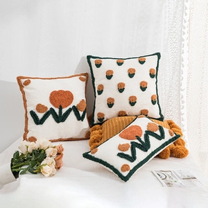 Detailed view of white boucle cushion covers with orange and dark green floral embroidery
