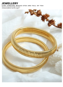 Detailed macro view of two gold-plated Tubogas stretch bracelets on white fabric