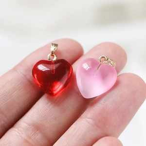Macro shot of red and pink jelly heart pendants with gold clasps on fingertips