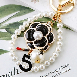 Macro view of pearl keychain with camellia flower, number five, and gold metal hardware