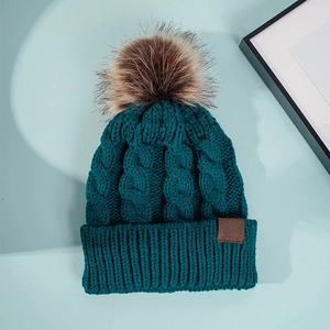 Detail of teal chunky knit beanie with a thick cable pattern and fluffy brown faux fur pom