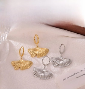 Detailed close-up of gold and silver ginkgo leaf hoop earrings on textured fabric