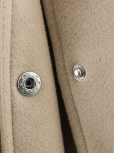 Macro detail of high-quality wool fabric texture and silver metal snap button on a beige jacket