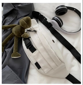 White canvas chest bag featuring a green plush frog charm and adjustable black strap
