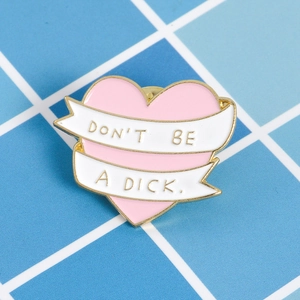 Detail of pink enamel heart pin with gold trim and white ribbon reading Don't Be A Dick