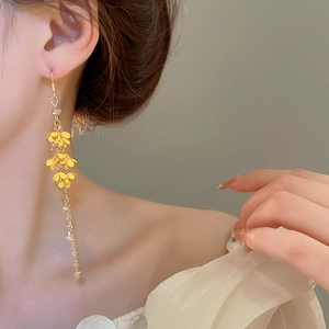 Close-up of long flower tassel earrings with yellow blossoms and gold chain on model