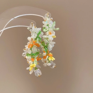 Detailed macro of handmade beaded earrings with white pearls and green crystals