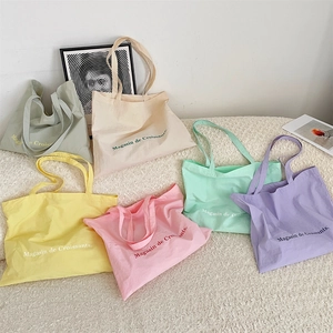 Detailed flat lay of large canvas tote bags in six pastel colors with French slogan print