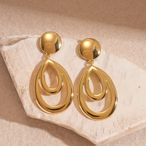 Macro shot of gold double-layered teardrop earrings on a textured stone surface