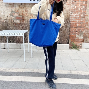 Blue canvas tote bag with large capacity shown in a street style handheld usage scene