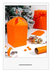 Macro shot of bright orange gift box with gold foil flecks and Christmas tree backdrop