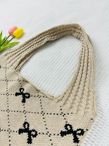 Detail of beige knitted tote bag featuring black argyle pattern and bow accents