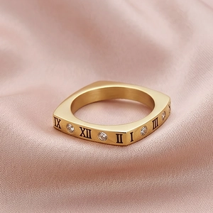Détail d'une bague carrée dorée avec chiffres romains et zircons sur soie rose
