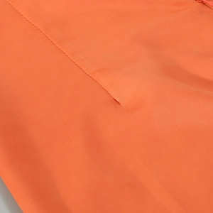 Detailed close-up of bright orange fine plain weave fabric and high-quality stitching detail