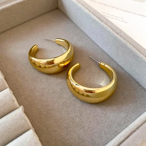 Macro shot of thick gold C-shaped hoop earrings with polished mirror finish on velvet tray