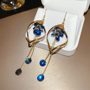 Dettaglio di orecchini geometrici dorati con cristalli blu e lunghe nappe a catenella