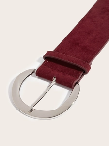 Détail macro d'une large ceinture en daim bordeaux avec boucle ronde en métal argenté