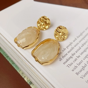 Gros plan de boucles d'oreilles dorées irrégulières avec pendentifs en résine marbrée