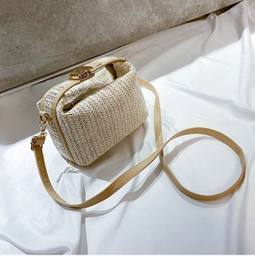 Detail of beige straw crossbody bag showing V-pattern weave and gold magnetic snap closure