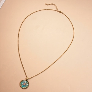 Détail du collier en bronze vintage avec pendentif mandala en verre sur fond beige neutre