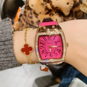 Detail of pink dial watch with rhinestone bezel and red clover charm bracelet worn on wrist