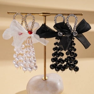 Elegant bow tassel earrings with faux pearls and rhinestones on a gold jewelry display