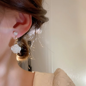 Detailed side view of floral acrylic camellia and faux pearl drop earrings on a model