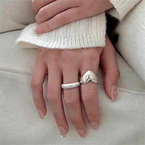 Close-up of a silver puffy heart ring and a textured croissant style band on a finger