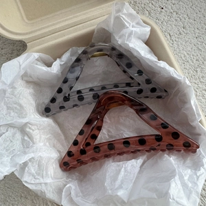 Detail of two triangle polka dot hair claws in black and amber colors on a beige tray