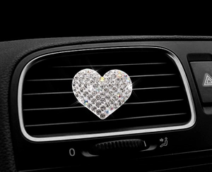 Close-up of heart-shaped rhinestone perfume clip on car air vent with sparkling finish