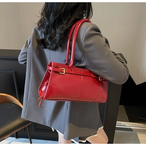 Detail of red glossy patent leather handbag with gold buckle and side tassels on model