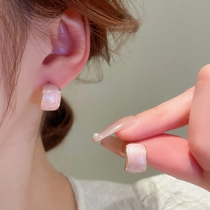 Pink glitter enamel C-shaped stud earrings with gold plating shown on ear and hand