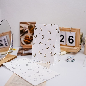 White paper gift bags with gold and silver bow patterns in flat and standing views