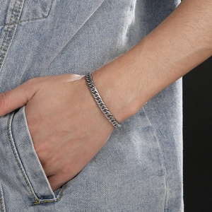 Gros plan d'un bracelet gourmette en acier titane argenté porté par un homme sur denim