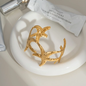 Bracelet jonc ouvert étoile de mer dorée style marin sur une assiette blanche en céramique