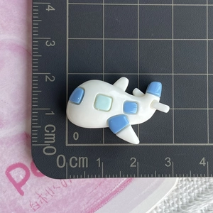 Detail view of a small resin cartoon airplane charm on a black measuring scale board