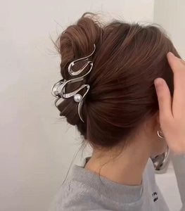Close-up of a silver liquid metal hair claw clip with a white pearl on a woman's hair