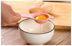 Pink egg separator in action separating egg yolk from egg white over a ceramic bowl