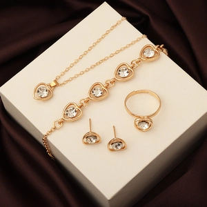 Golden heart jewelry set with clear crystals displayed on white stand over silk background