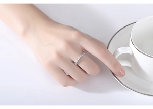Close-up of minimalist silver bezel-set zircon ring worn by model holding a white teacup