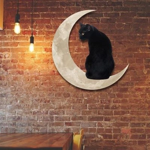 Artistic black cat sitting on moon metal wall decor on a rustic red brick wall