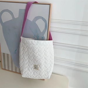 Detail of white heart-quilted shoulder bag with purple strap and branded fabric label