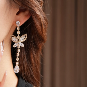 Close-up of a model wearing gold butterfly drop earrings with sparkling zircon crystals
