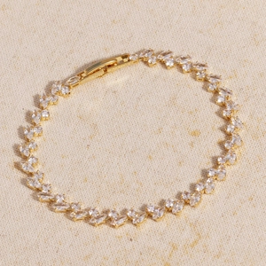 Detail of gold zircon bracelet with marquise-cut stones on warm fabric texture background