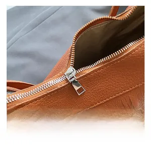 Detailed close-up of brown lychee leather bucket bag with silver metal zipper and tassel deco